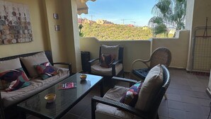 Ein Balkon mit einer Couch, Stühlen, einem Tisch und Blick auf eine hügelige Landschaft.