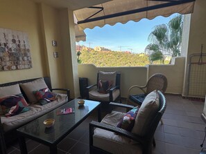 A balcony with a sofa, chairs, a table, and a view of a hilly landscape. - Beautiful apartment 85m2, with terrace in a +++ site, 5 swimming pools; 1 k from the sea (Manilva)