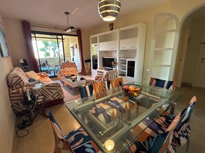 A living room with a glass dining table, patterned sofas, and a white entertainment unit. - Beautiful apartment 85m2, with terrace in a +++ site, 5 swimming pools; 1 k from the sea (Manilva)