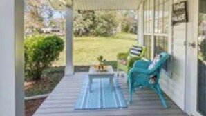 Un porche cubierto con mesa y sillas, vista a un patio césped, y una puerta con un letrero.