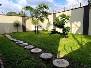 Ein Garten mit gepflastertem Wegweiser, Palmen und einem Gebäude mit schmiedeeisernem Zaun.