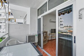 Ein Balkon mit Glastür, einem weißen Stuhl, einem kleinen Tisch und einem Fernseher im Hintergrund.