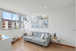 Una sala de estar moderna con un sofá gris, mesitas auxiliares, una lámpara de pie y una obra de arte en la pared.