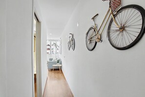 Un pasillo con una bicicleta colgada en la pared, una pequeña mesa redonda con una planta y un sofá al fondo.