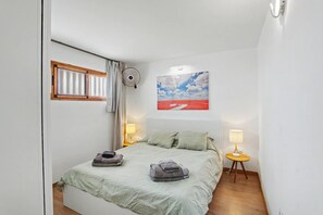 Una camera da letto con un letto, due lampade sui comodini, una finestra con tende, un ventilatore a parete e un quadro.