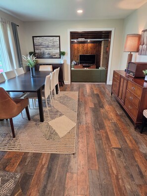 A dining area with a table and chairs, a TV in the background, and a wooden floor. - Spacious 4 bdr house in Medinah within walking distance of Medinah Country Club (Medinah)