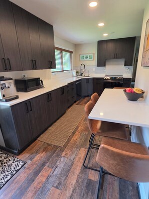 A modern kitchen with dark wood cabinets, a white countertop, a stainless steel sink, and a dining area with a white table and brown chairs. - Spacious 4 bdr house in Medinah within walking distance of Medinah Country Club (Medinah)