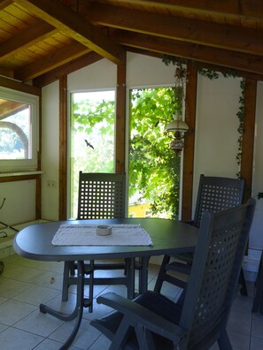 A dining area with a table and chairs, a window with a view of greenery, and a hanging light fixture. - Quiet vacation apartment on the edge of the forest with panoramic views directly on hiking trails (30 m) (Prümzurlay)