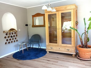 A room with a wooden cabinet, a blue rug, a chair, a cat tree, and a potted plant. - Quiet vacation apartment on the edge of the forest with panoramic views directly on hiking trails (30 m) (Prümzurlay)