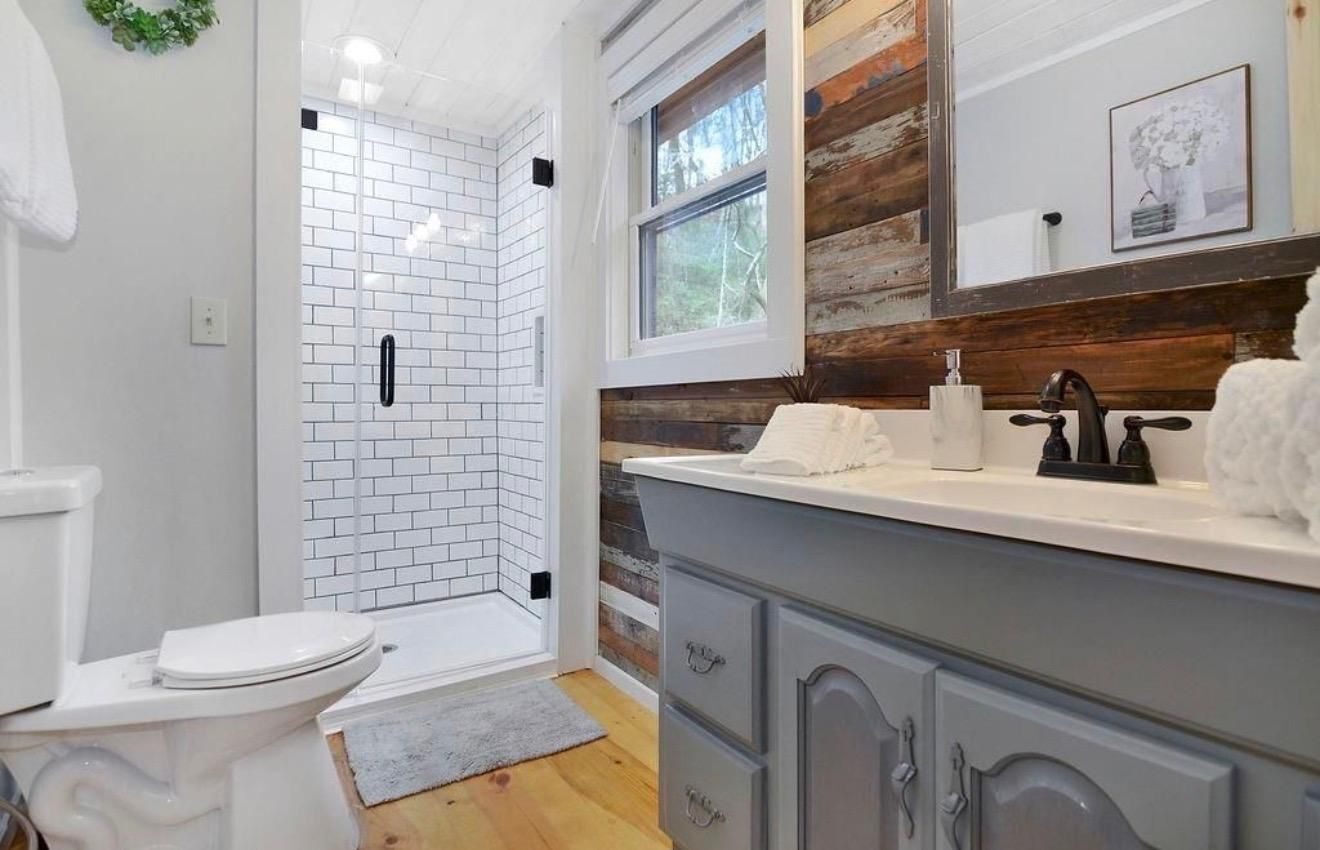 A bathroom with a white toilet, a shower with white tiles, and a vanity with a mirror and sink.