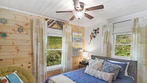 Ein Schlafzimmer mit Bett, Deckenventilator, Fenster und Stuhl.