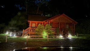 Eine Holz-Blockhütte mit Veranda, einem kleinen Garten und einem Teich.