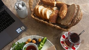 A laptop, a basket of bread, a plate with cheese, tomatoes, and olives, and a glass of drink on a table. - Kale Otel Bodrum (Bodrum)