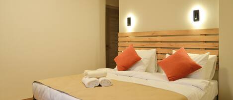 A hotel room with a bed, two wall-mounted light fixtures, and a door leading to another room.