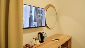 A television mounted on a wall, a wooden table with a kettle, two water bottles, and a remote control. - Kale Otel Bodrum (Bodrum)