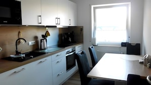 Una cocina moderna con armarios blancos, un microondas negro, un hervidor y un ventanal con vistas.
