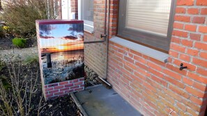 Ein Backsteinhaus mit Fenster, eine kleine Außenanlage mit Pflanzen und eine Metallkonstruktion mit Blick auf den Sonnenuntergang.