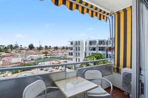 Ein Balkon mit Tisch und Stühlen, Blick auf die Stadt und ein Pool im Hintergrund.