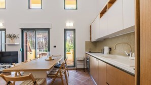 A modern kitchen with wooden cabinets, a dining area with a table and chairs, and a view through the glass doors. - Villa Dita Qerret | Relaxing Beachfront Stay by PikHost (Qerret)