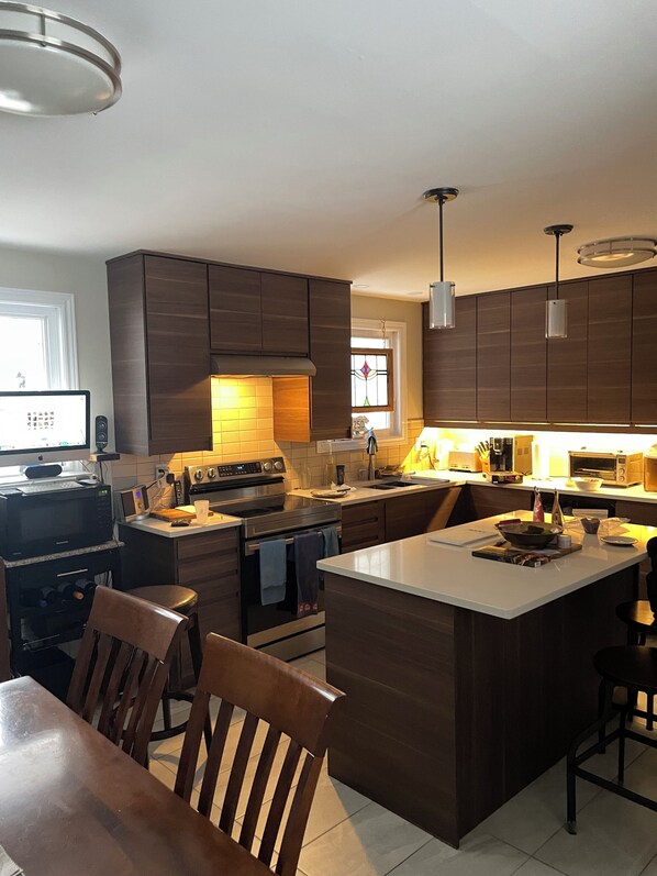 Una cocina moderna con armarios de madera oscura, una isla central, una mesa de comedor con sillas y un horno empotrado.