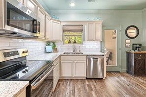 A kitchen with a stainless steel oven, a dishwasher, and a window with a view of trees.