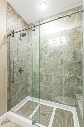 A glass-enclosed shower with a control panel, a handrail, and a tiled wall.