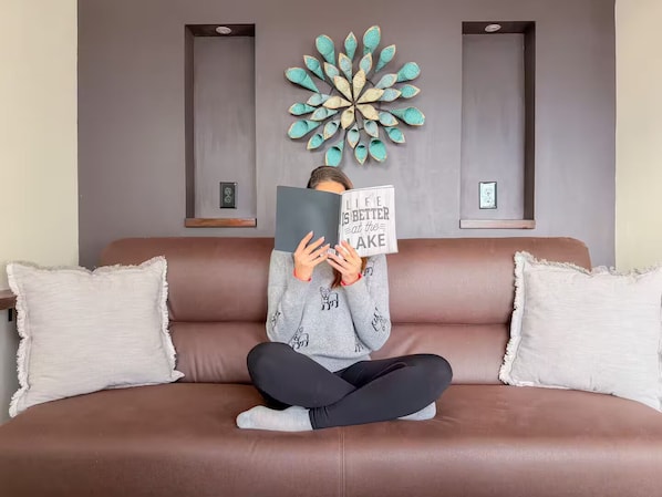 Une personne est assise sur un canapé en cuir marron, avec deux coussins blancs, et tient un livre contenant une citation inspirante.