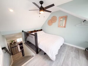 Quarto com cama, ventilador de teto, escada, área de cozinha e espelho.