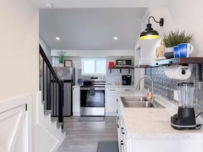 Une cuisine moderne équipée d’appareils électroménagers en acier inoxydable, d’un four encastré, d’un four à micro-ondes, d’un évier et d’un plan de travail avec un mixeur.