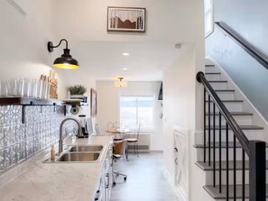 Cozinha com bancada de mármore, pia de aço inoxidável e luminária pendente preta.