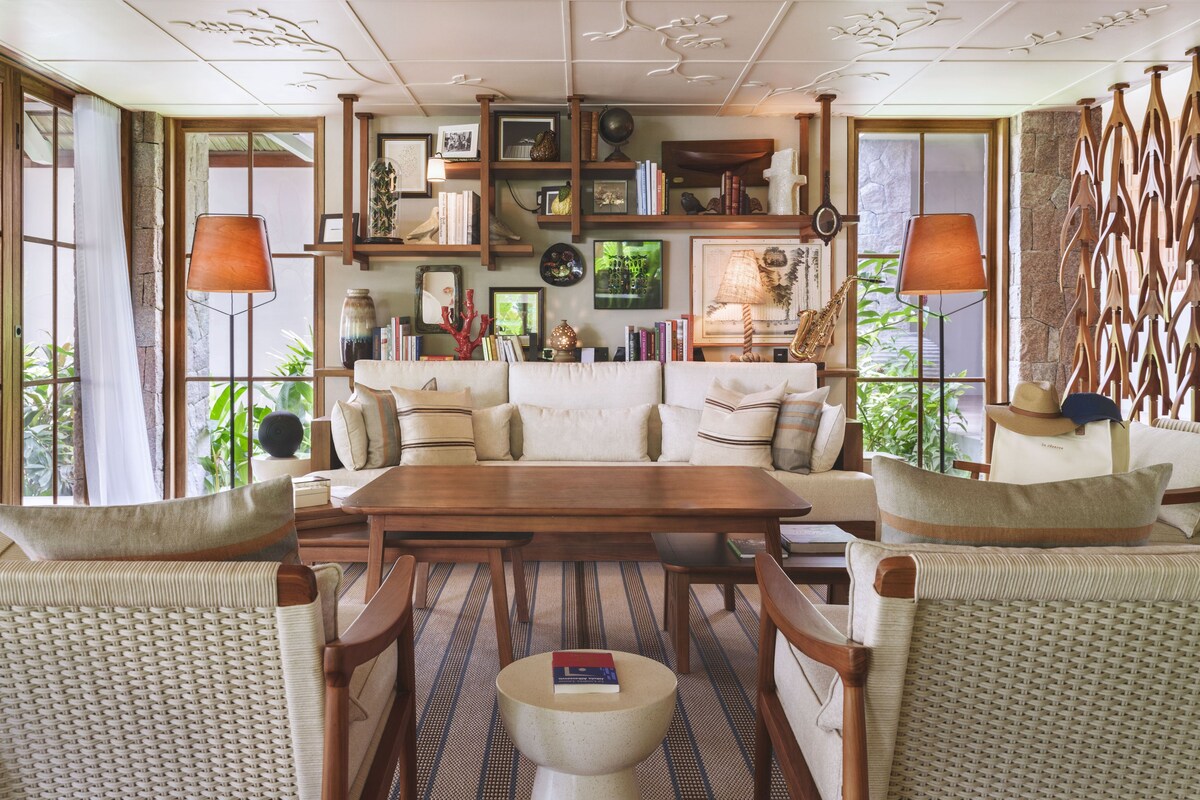 Una habitación con una mesa de comedor de madera, sofás con cojines y una estantería llena de libros y objetos decorativos.