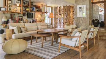 A cozy living room with a wooden coffee table, a sofa, and chairs. There is a bookshelf filled with books and decorative items.