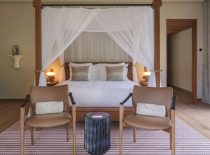 Una habitación de hotel con una cama con dosel, dos mesitas de noche con lámparas, una pequeña mesa redonda y dos sillones.