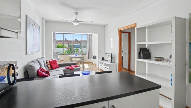 Een moderne keuken met een centraal eiland, een eethoek met een tafel en stoelen, een witte inbouwkast en uitzicht op de omgeving.