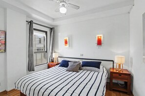 Un dormitorio con una cama, dos mesitas de noche con lámparas, una ventana con cortinas y un ventilador de techo.