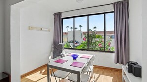 Een kamer met een eettafel, stoelen, een raam met gordijnen, een plafondlamp en uitzicht op het omliggende landschap.