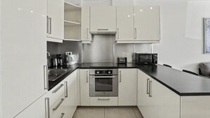 Een moderne keuken met witte kasten, een oven van roestvrij staal, een zwart aanrecht en een magnetron.