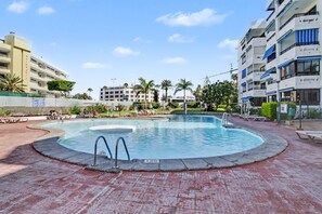 A swimming pool with a circular design, surrounded by a brick walkway, and adjacent to a multi-story building with balconies. - Vacation Apartment 'Iguazu Yumbo - Two Bedroom Apt' with Wi-Fi (Maspalomas)