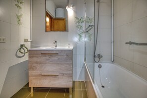 Un baño con tocador de madera, lavabo, espejo, ducha y paredes con azulejos.