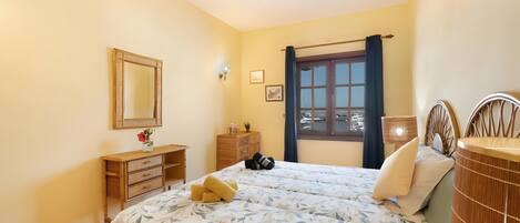 A bedroom with a bed, a ceiling fan, a dresser, a mirror, and a window with curtains.