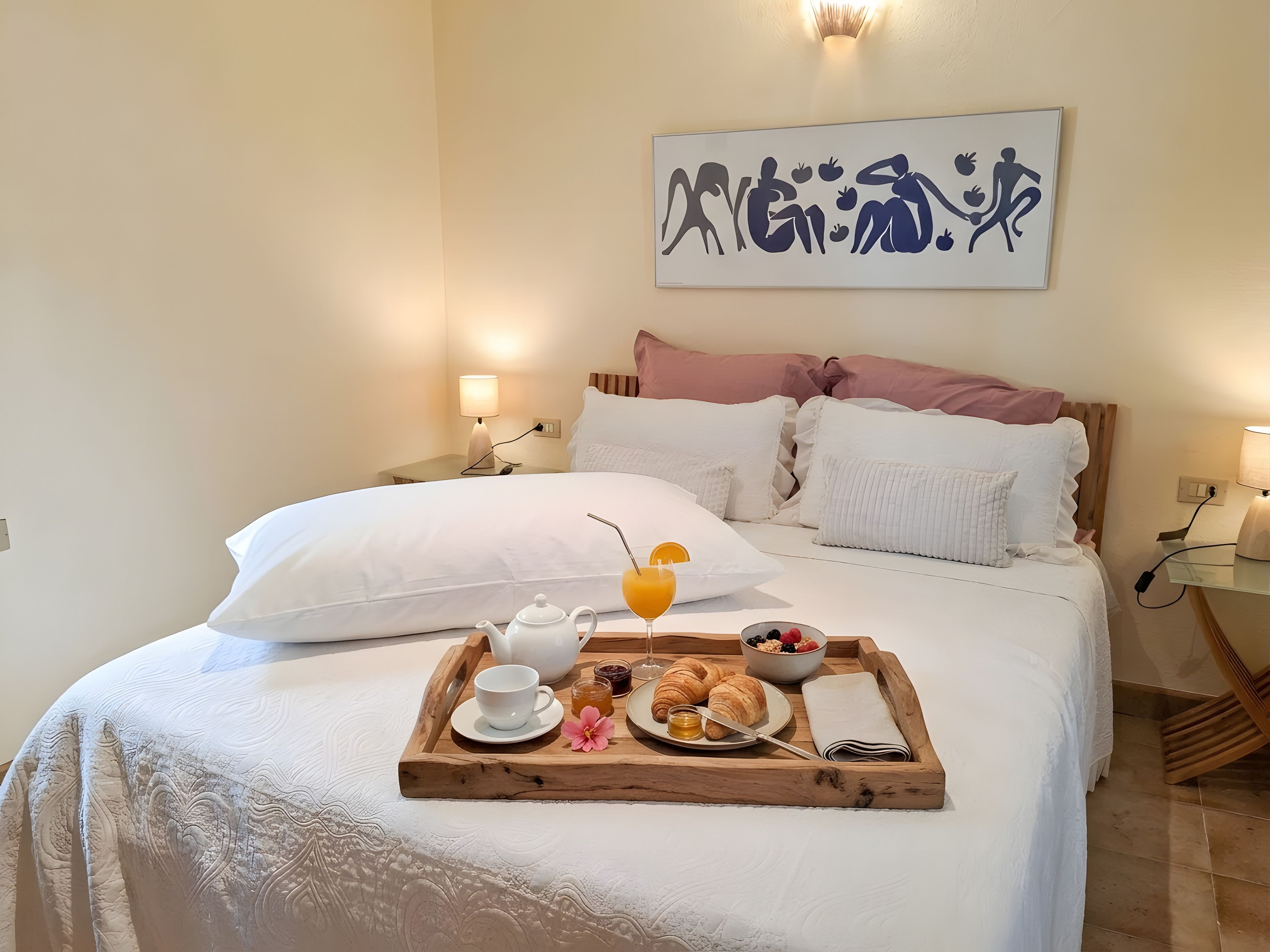 Una cama bien hecha con una bandeja de desayuno que incluye croissants, fruta y un vaso de jugo de naranja.
