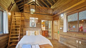 Ein Schlafzimmer in einer Holzhütte mit Bett, einer Leiter und einem Fenster mit Blick.