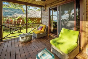 A wooden deck with wicker furniture, a thatched roof, and a view of greenery.