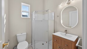 Ein Badezimmer mit Duschkabine, Toilette, Waschbecken und Spiegel sowie einem Fenster.