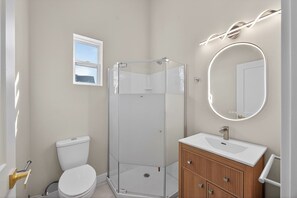 A bathroom with a glass shower enclosure, a toilet, a sink with a mirror, and a window.
