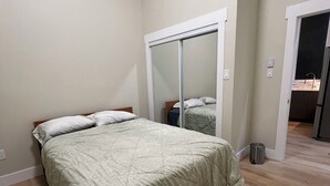 Ein Schlafzimmer mit einem Bett, einem Spiegel, einer Tür und einem Mülleimer.
