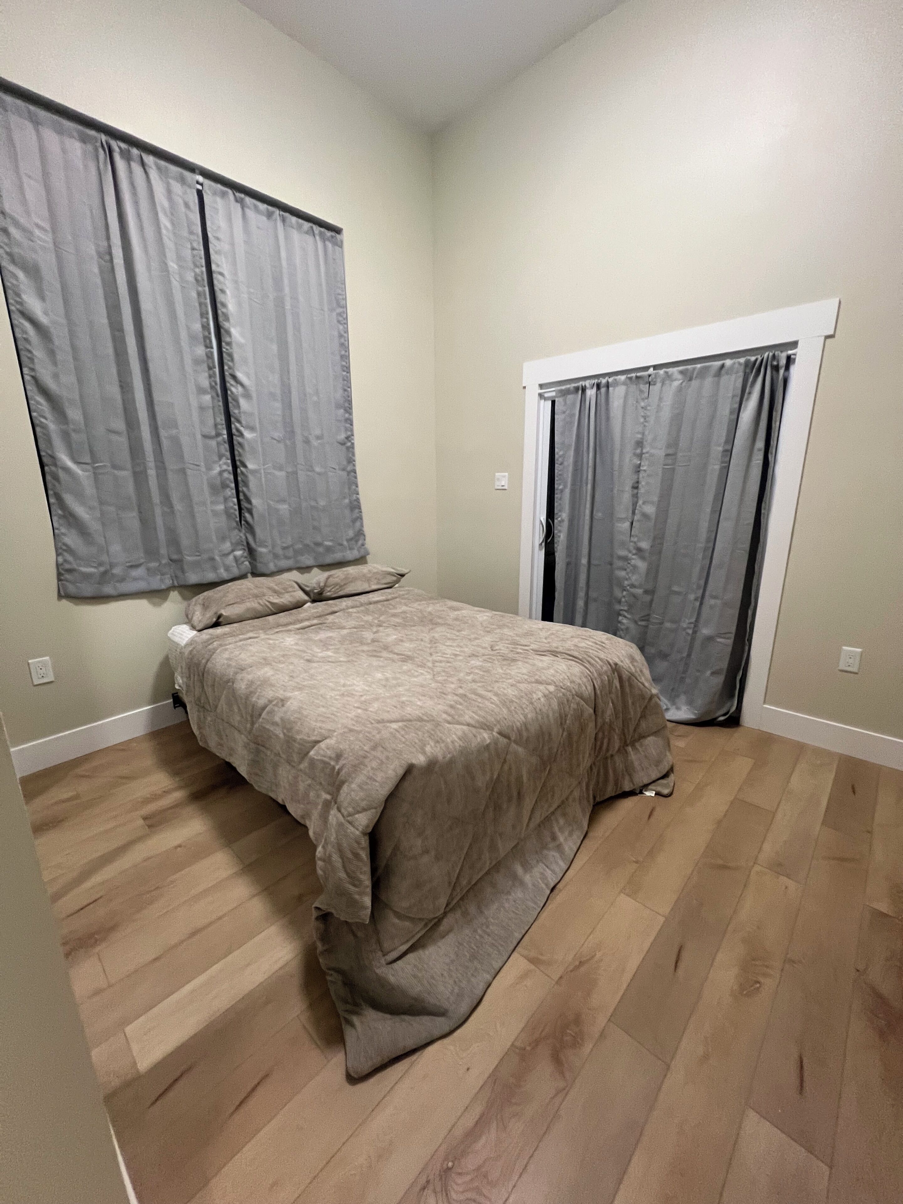Una camera da letto con un letto, due finestre con tende, una porta e pavimento in legno.