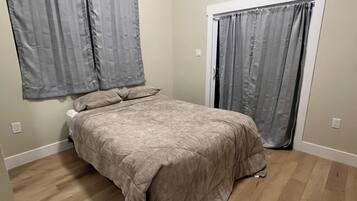Una camera da letto con un letto, due finestre con tende, una porta e pavimento in legno.