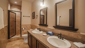 Een badkamer met twee wastafels, toilet, douche en handdoekhouder.