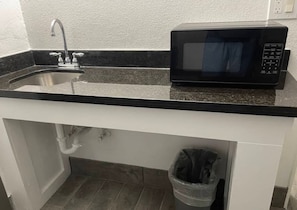 A kitchen with a black countertop, stainless steel sink, and a black microwave.